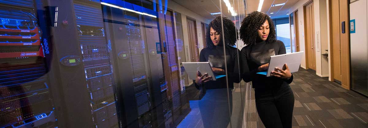 Woman looking at tablet leaning on glass overlooking data center racks