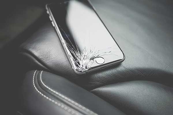 iphone with cracked screen on black leather car seat