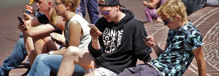 young people sitting on the sidewalk and looking at their smartphones