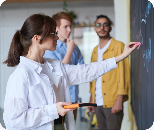 woman in white blouse writes with chalk on chalkboard