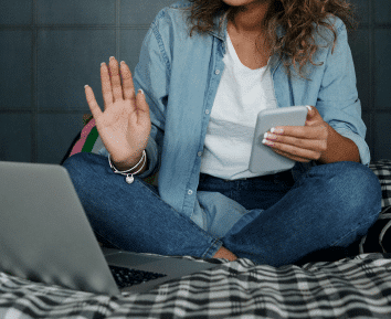 woman sitting on her bed with laptop and mobile phone