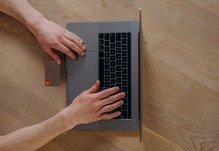 hands on macbook with card on wooden floor