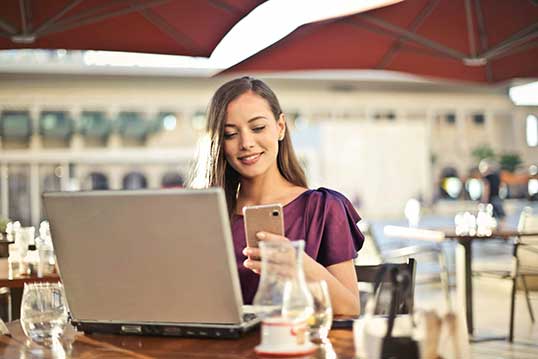 Smiling woman looking at phone at table with laptop