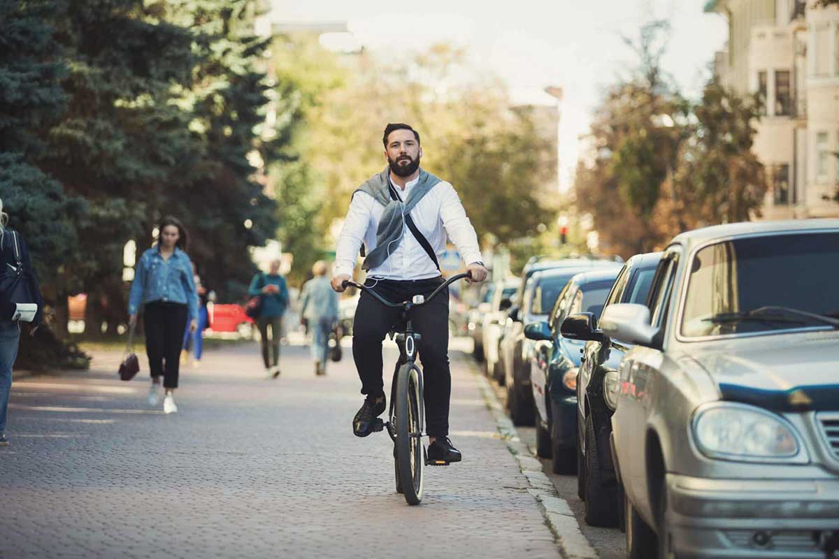 Young businessman going to work on bike on sidewalk near cars and people